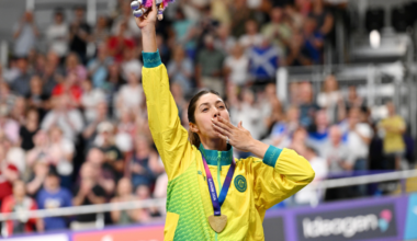 Female athlete in a yellow-green jersey raises a trophy and kisses her medal amid a cheering crowd.