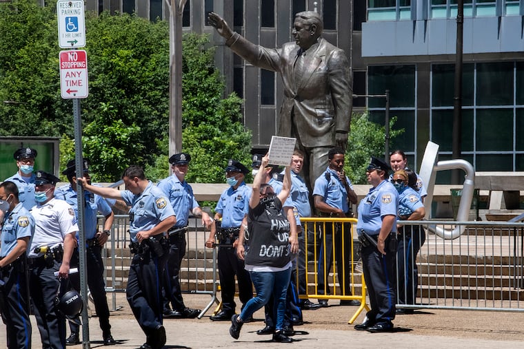 A protester walks near the Frank Rizzo statue as Philadelphia police guards the area during a protest in 2020.