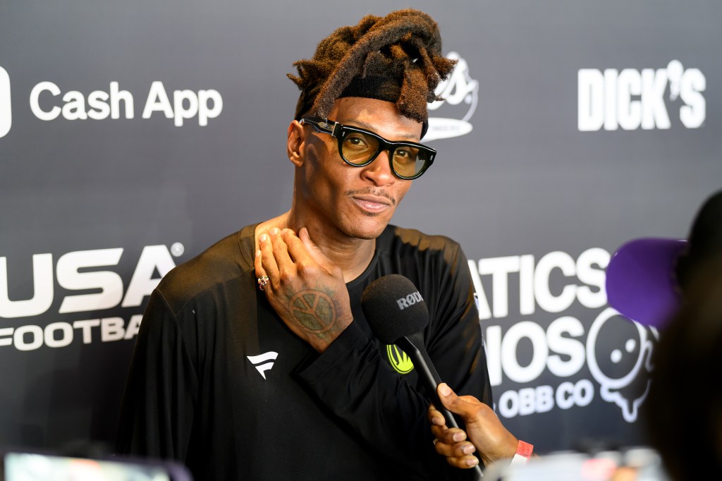 A man with dreadlocks and sunglasses speaking into a microphone.