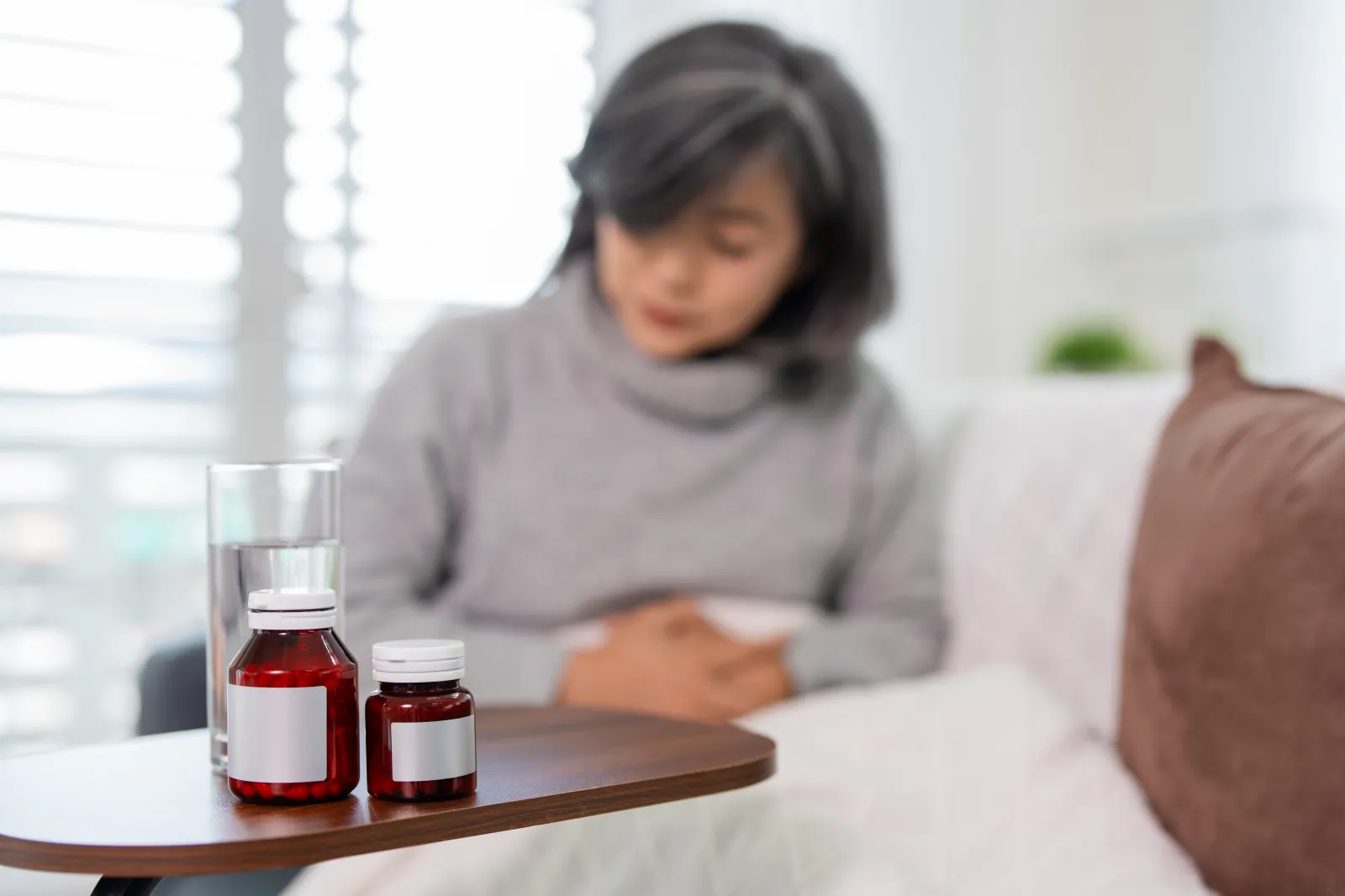 A stock image shows a woman with a bottle of pills, suffering from abdominal pain.