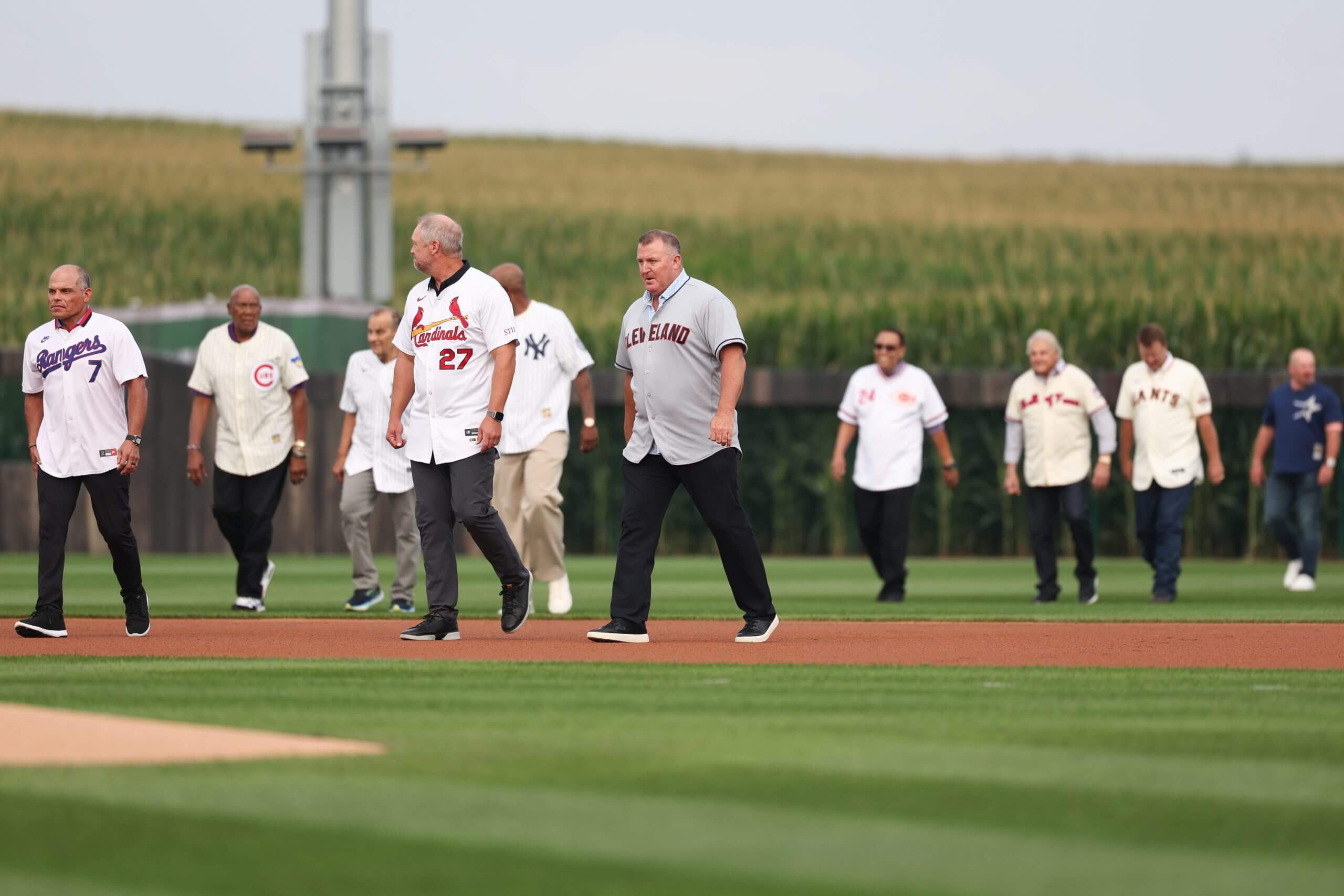Hall of Fame players wearing baseball jerseys walk from the corn to the infield.
