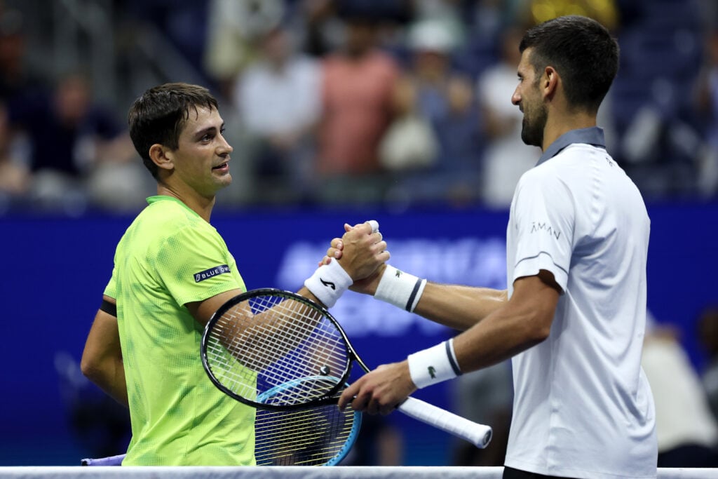 Mariano Navone of Argentina embraces Novak Djokovic of Serbia after their Men's Singles First Round match