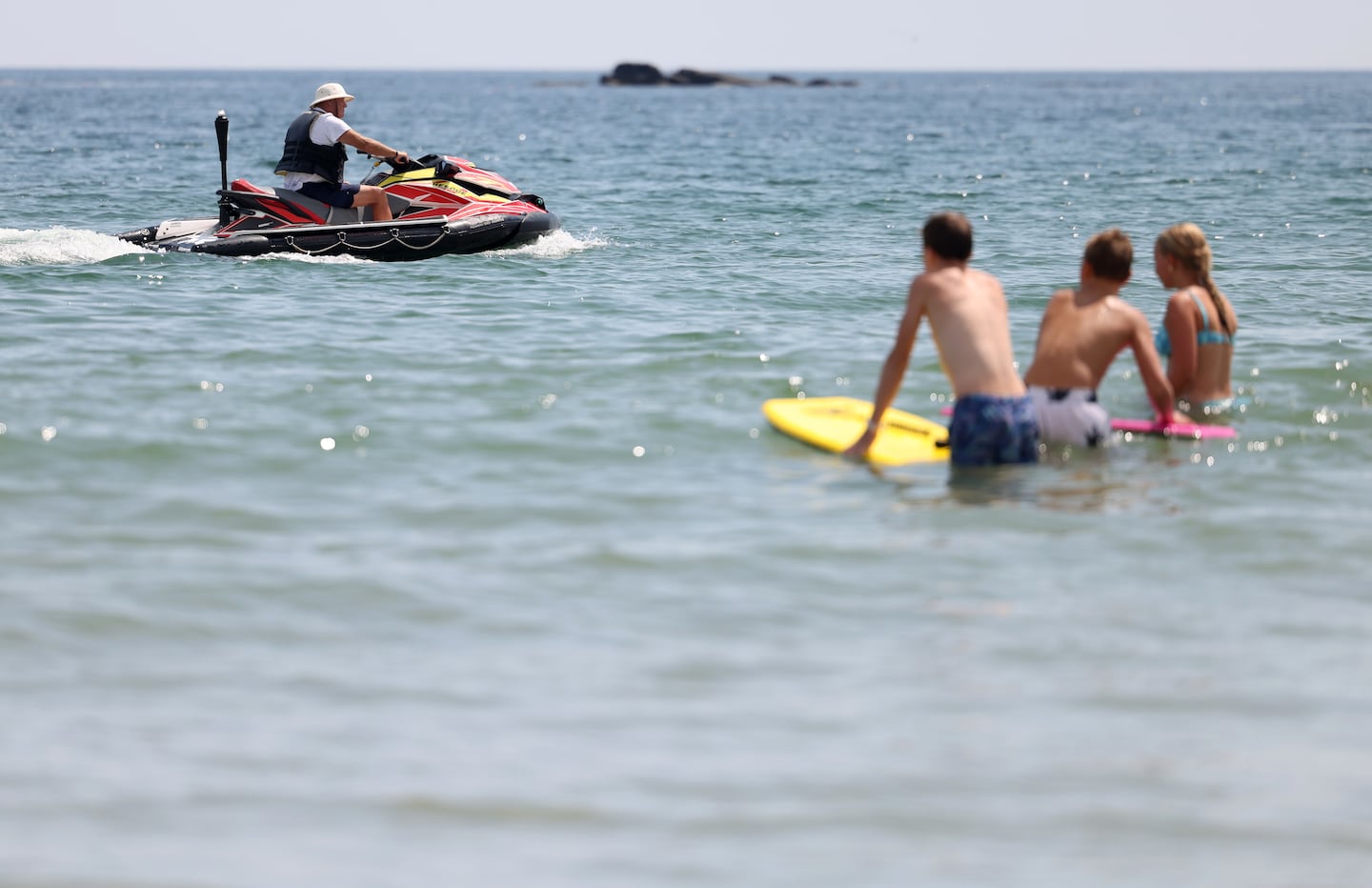A jet ski used to scare away sharks passes by a group of kids boogie boarding.