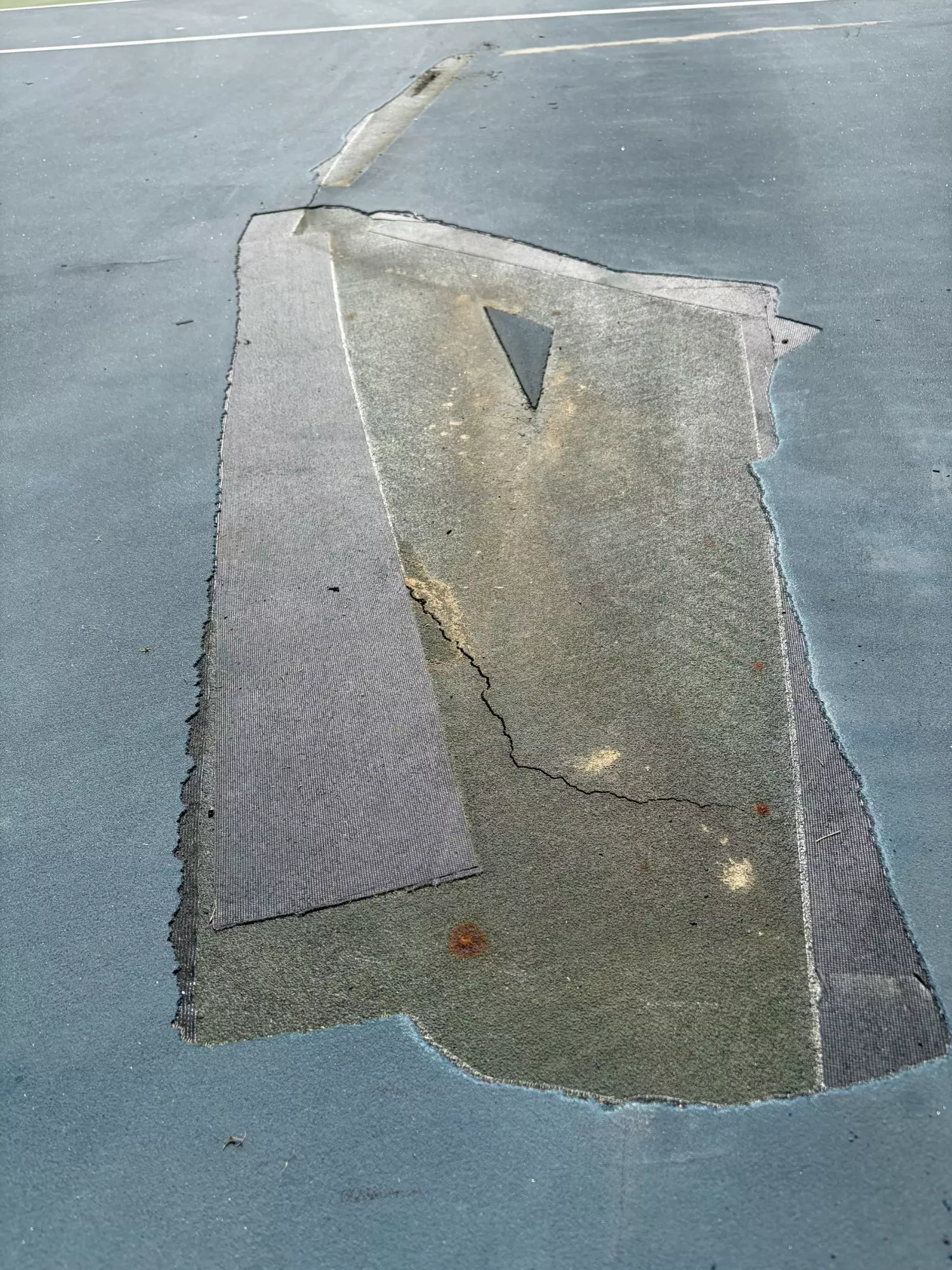 Close-up of a large damaged and previously repaired section of the tennis court surface at the Nisbet Tennis Center before resurfacing.