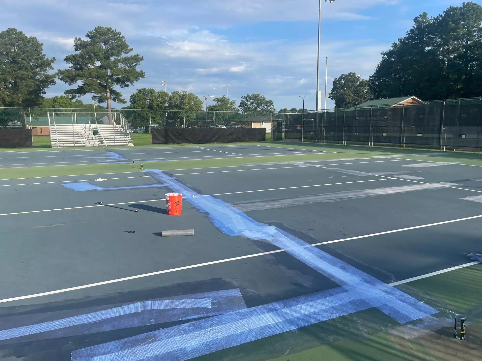 Wide view of the Nisbet Tennis Center during resurfacing, with multiple repaired and sealed cracks visible across the courts.