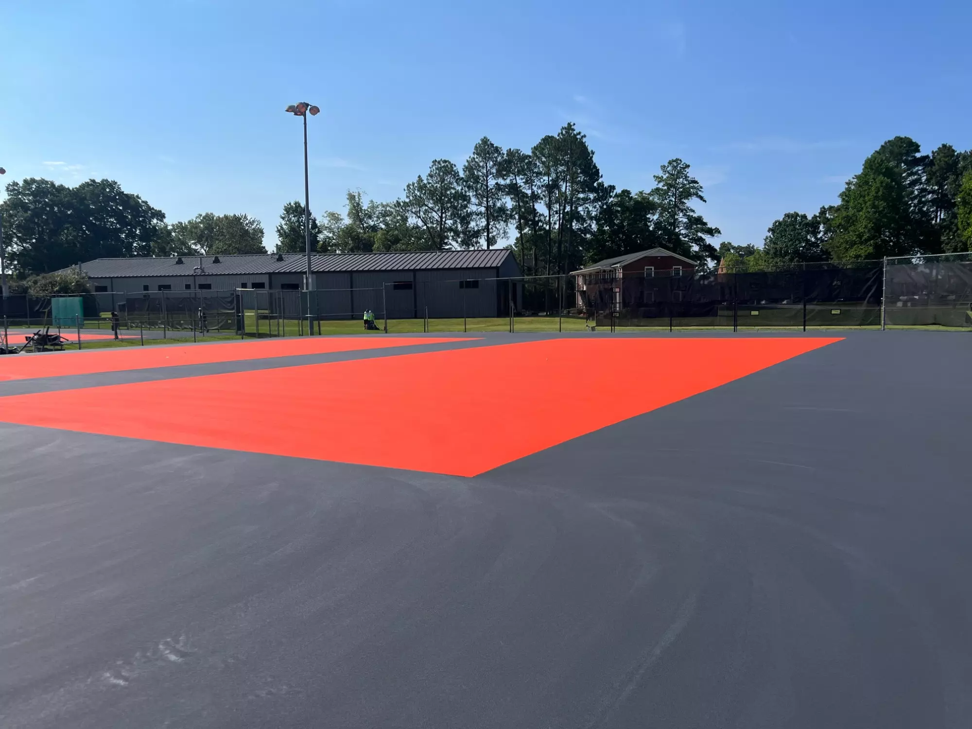 A Nisbet Tennis Center court receives its new bright orange and slate gray surface during the resurfacing project.