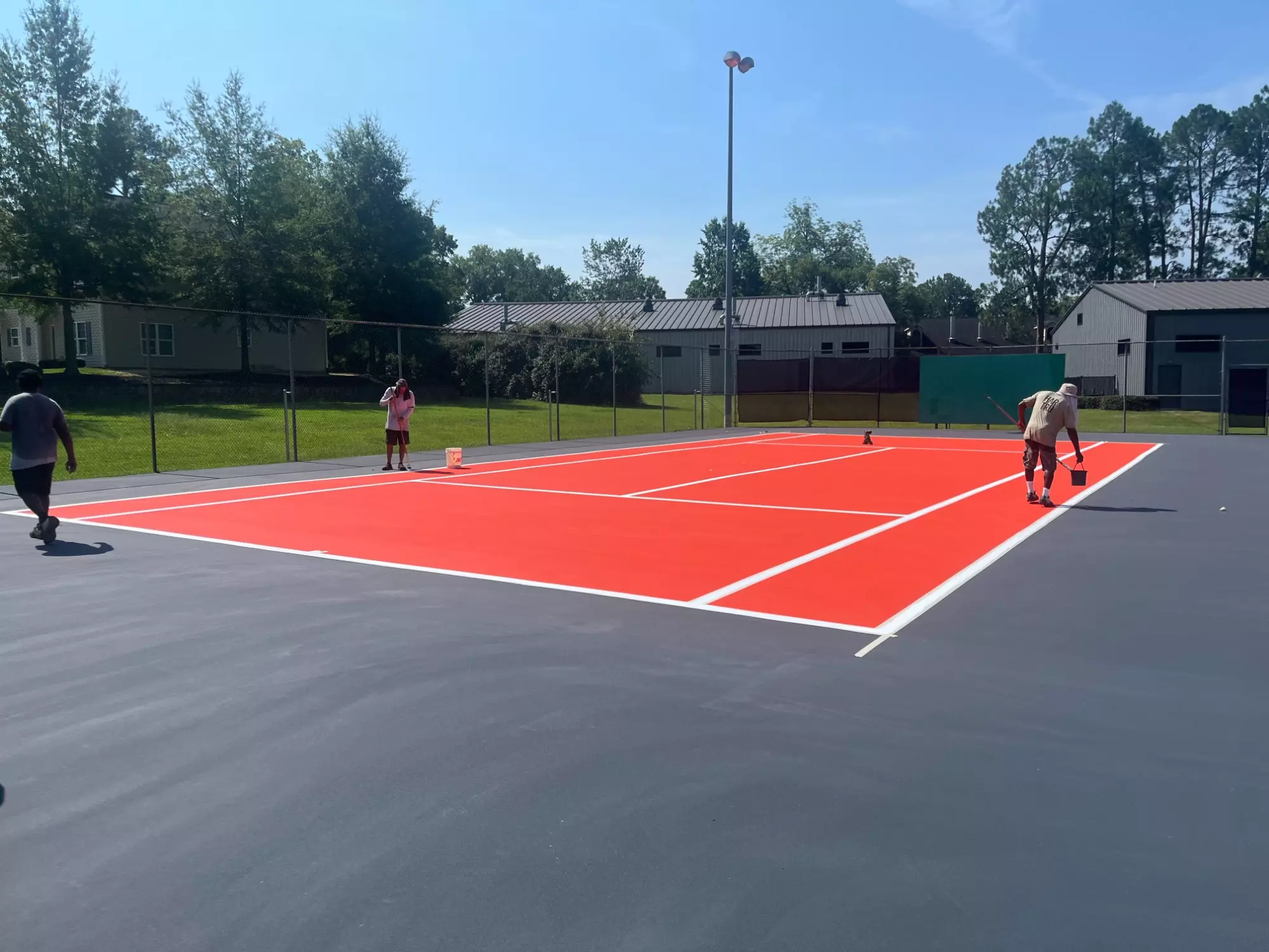 World Class Courts crew members work on the finishing touches of a newly resurfaced orange and slate gray court at the Nisbet Tennis Center.