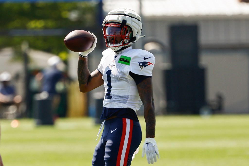 New England Patriots player wearing a white jersey with a number one, white padded helmet, and blue pants with red and white stripes, holding a football.