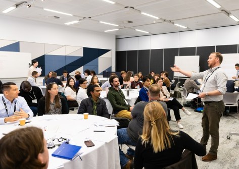 A group of young and emerging professionals seated at round tables in a conference room