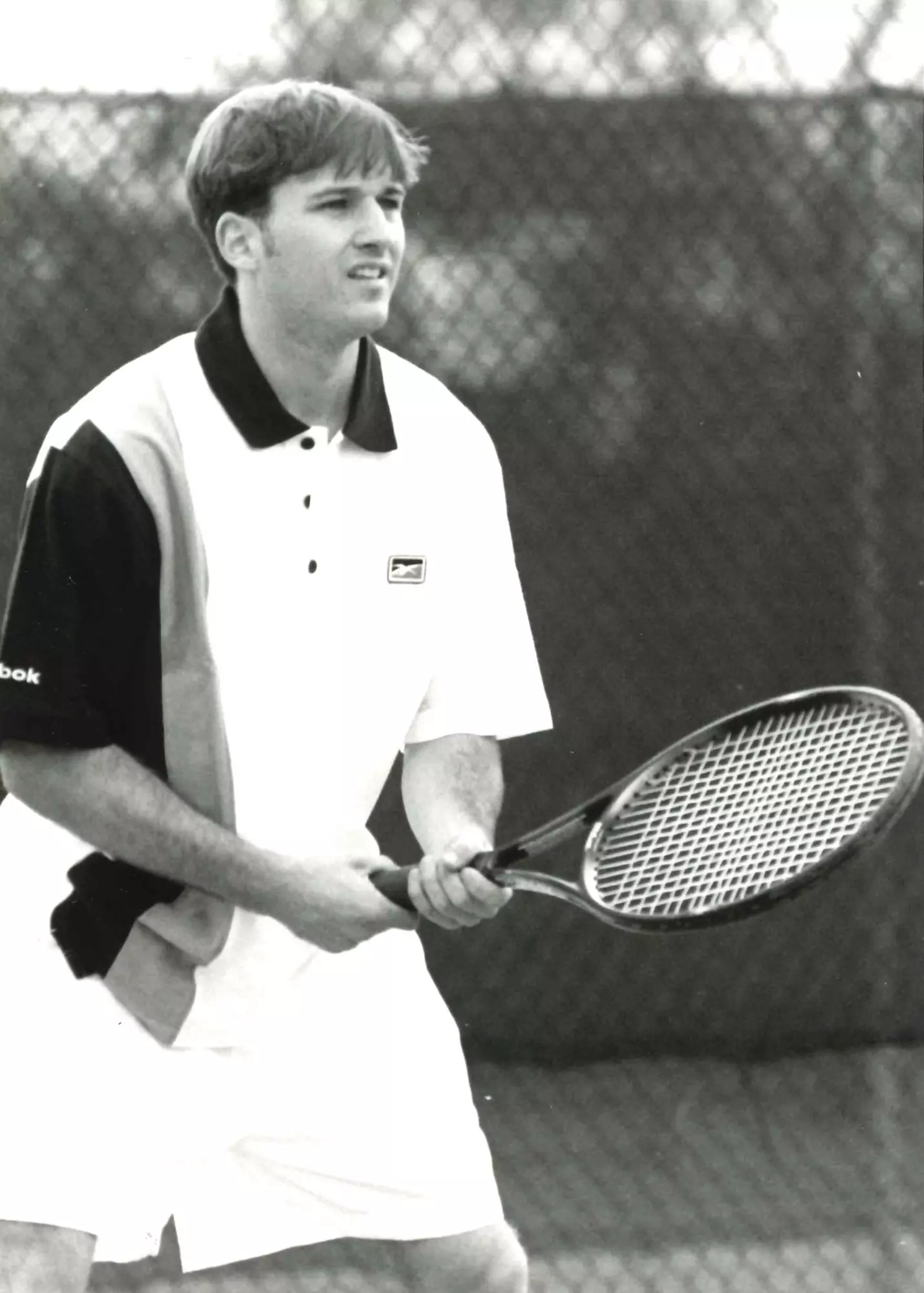 A man holds a tennis racket with both hands while looking ahead.