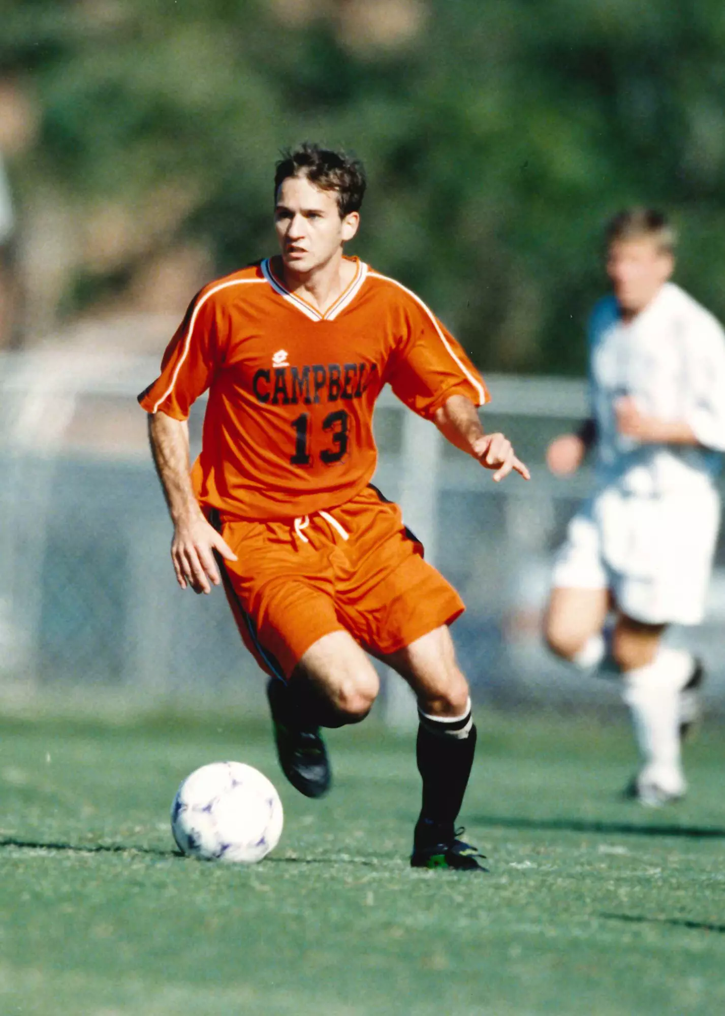 A soccer player wearing a jersey with Campbell #13 dribbles a soccer ball while looking up.