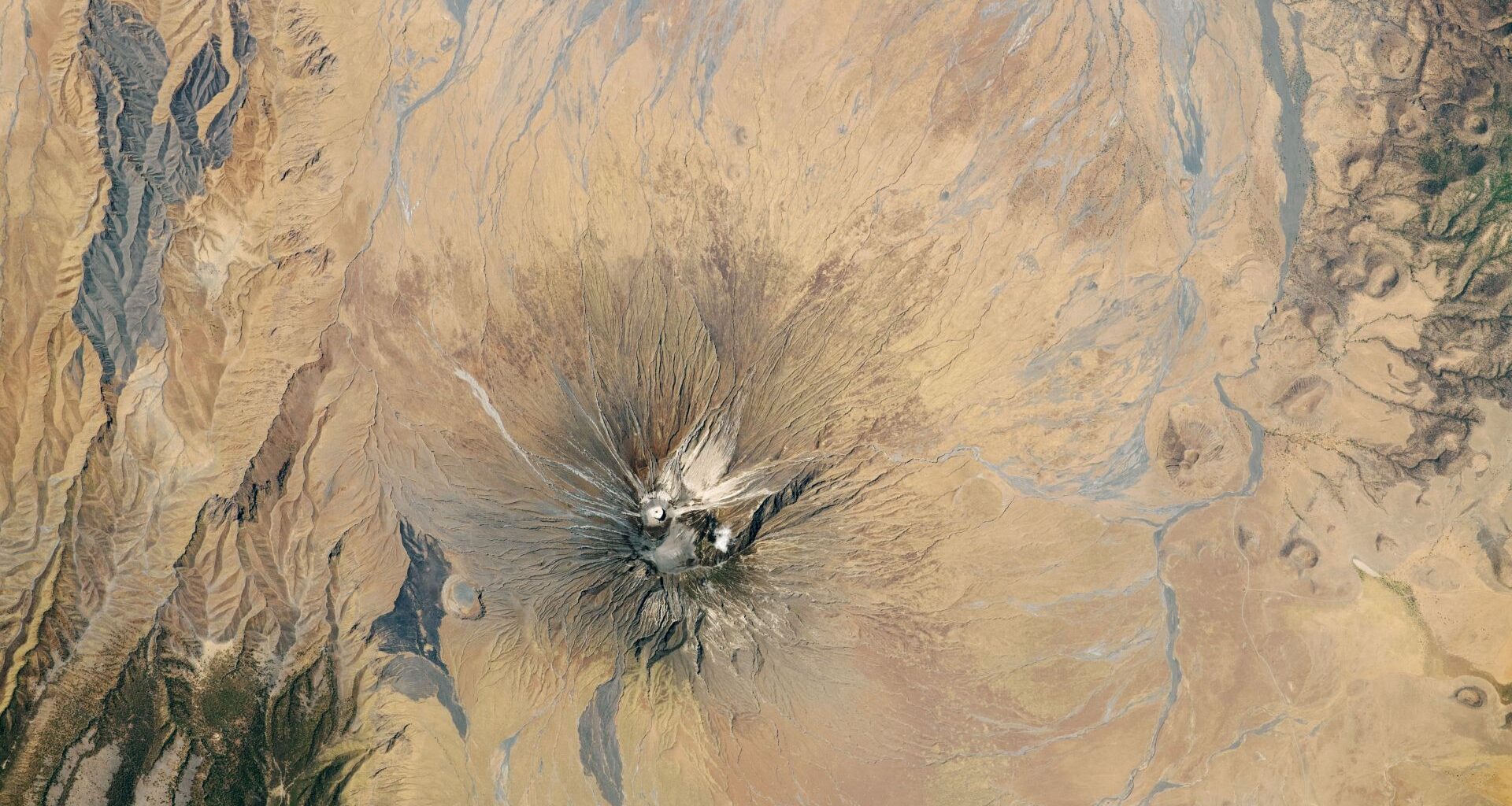 Satellite picture of a dry region with a volcano capped with white ash