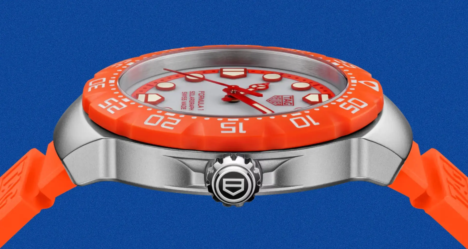 Silver TAG Heuer Formula 1 watch with orange bezel and strap on blue background.