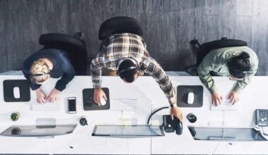 Looking down on a workstation with three people working on their tech devices.