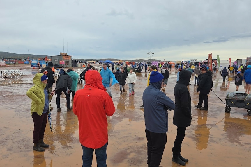 People walking around at festival site with muddy puddles and water wearing rain gear