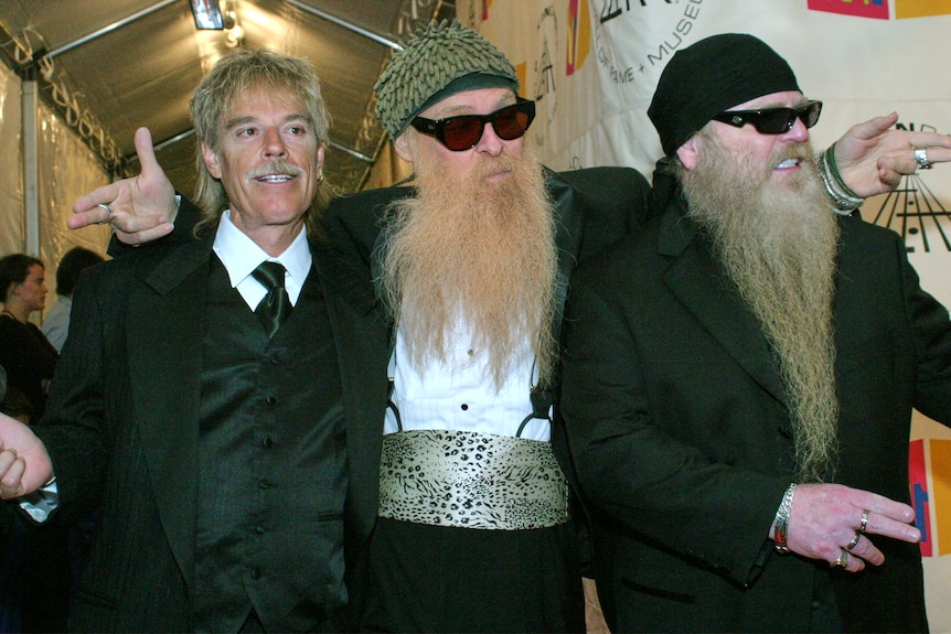 Three members of ZZ Top pose on a red carpet. 