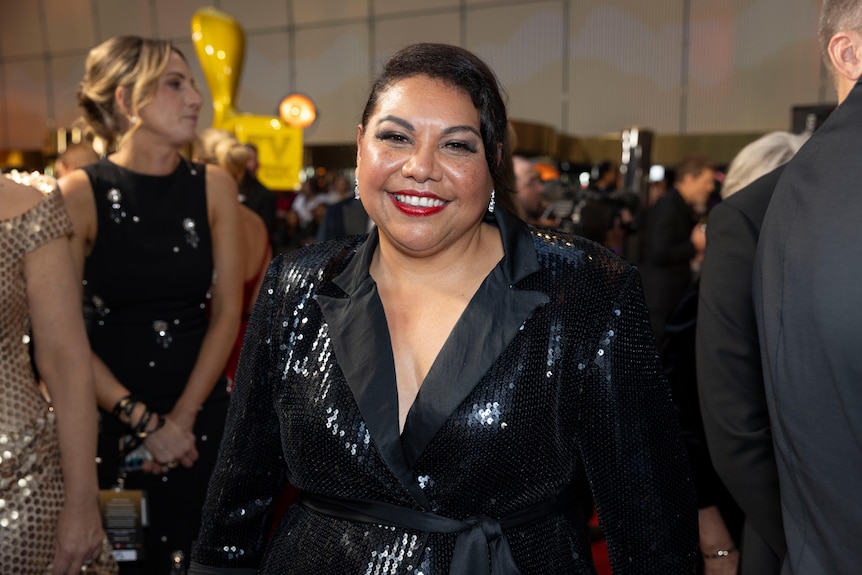 Mailman, wearing a sequined black blazer cinched at her waist, smiles.
