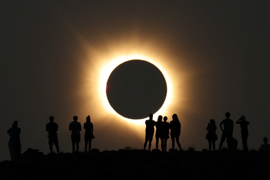 A group of people in front of a total solar eclipse.