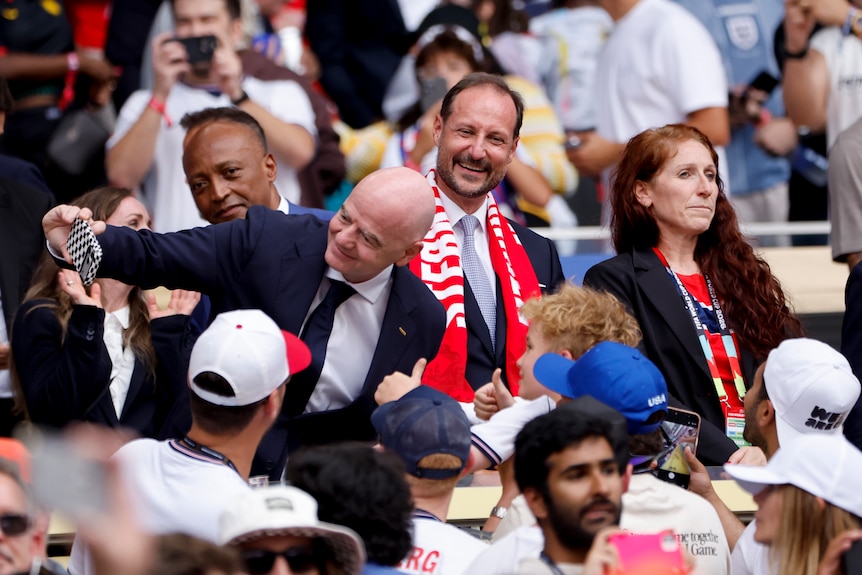 A man in a suit takes a selfie with a child, while a woman in a Norway scarf looks on.