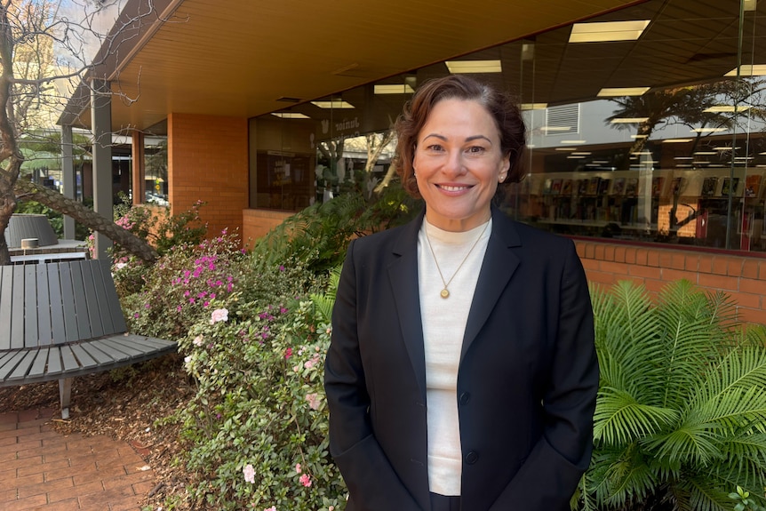 A woman with short brown hair and brown eyes smiles at the camera. She is wearing a white shirt and black blazer.