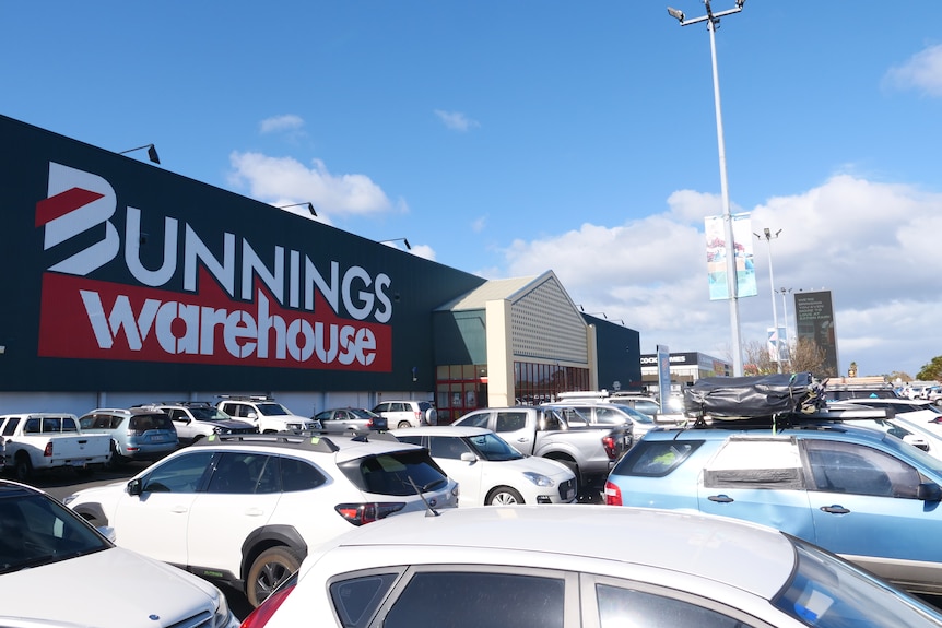 The outside of a Bunnings store, large warehouse building with lots of cars in the carpark.