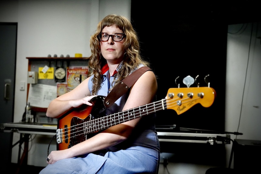 A woman with cool glasses sits holding a guitar.
