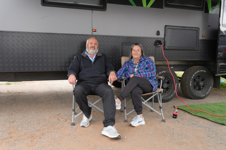 Couple sits on fold up chairs in front of caravan.