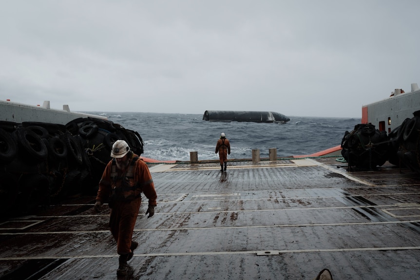 A rocket is seen floating in the ocean from the deck of a ship which has two crew members on board