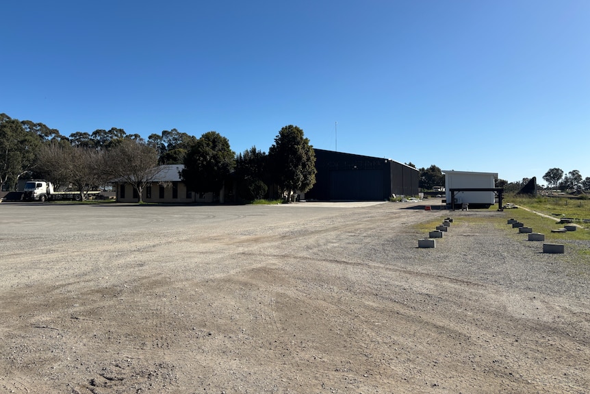 Image of gravel area, trees and warehouse building
