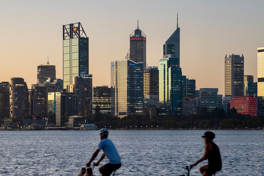 Skyscrapers in the background with the Swan River in the middle and two bicycle riders in the foreground.