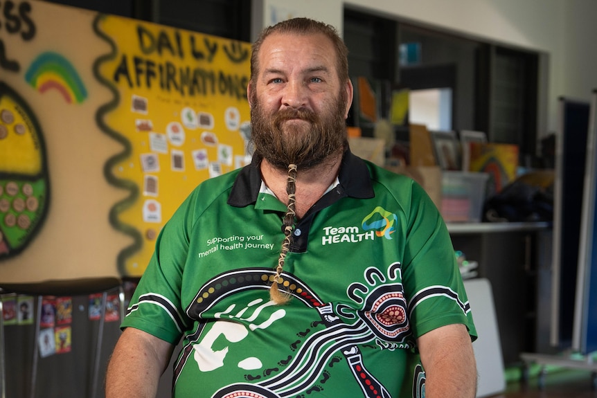 Spike has a long beard, wrapped into a thin ponytail with string, the man wears a green TeamHEALTH shirt and smiles.
