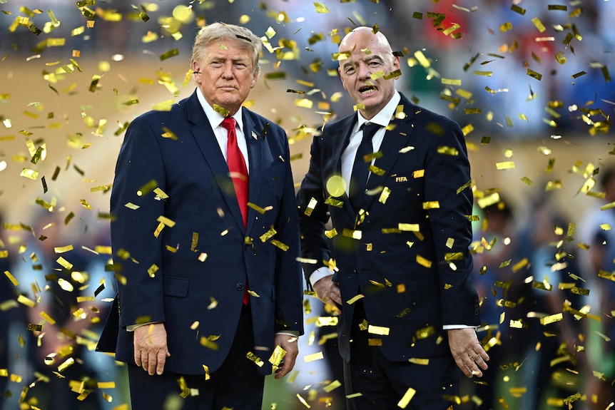Donald Trump and Gianni Infantino standing while wearing suits amid falling goldens trips of confetti.