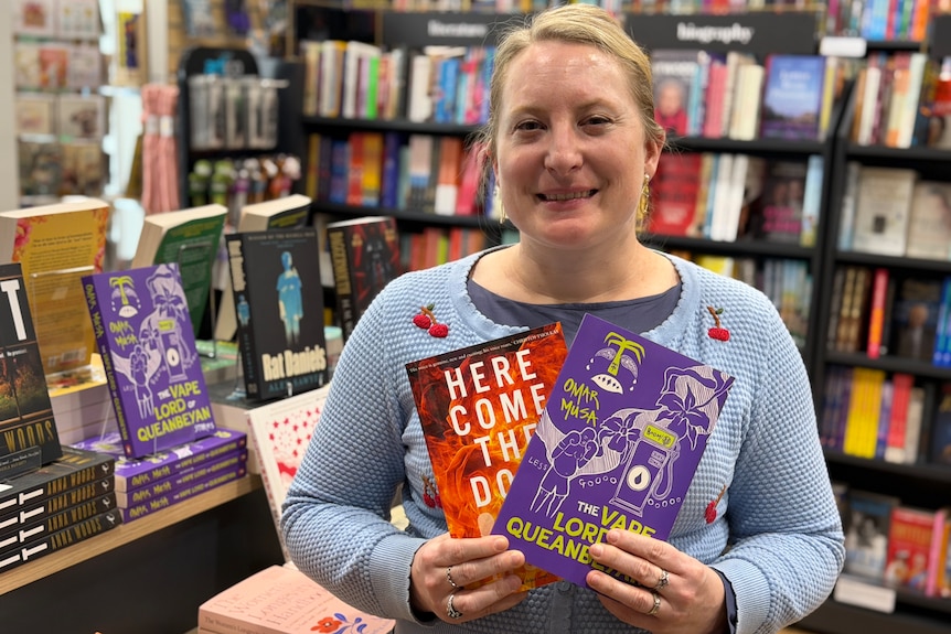 A bookshop owner holds up two novels.
