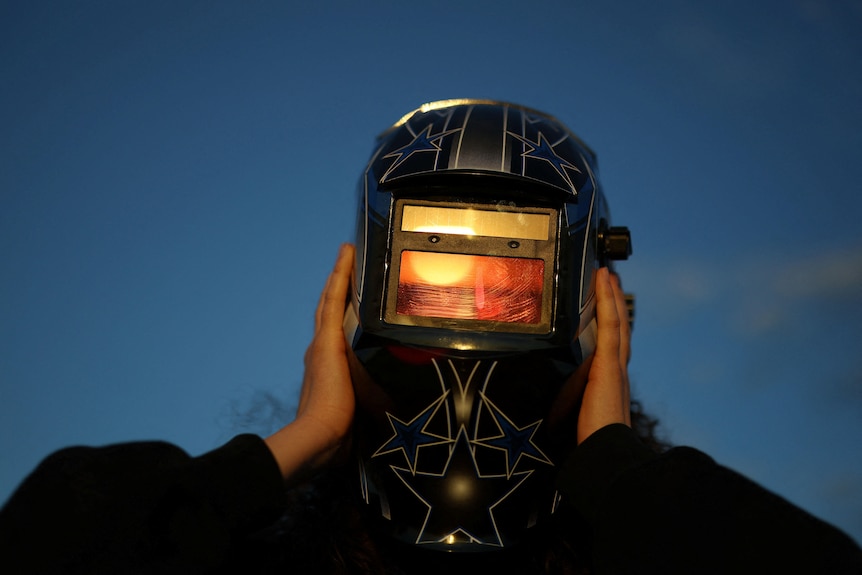 A woman wearing a welder's mask.