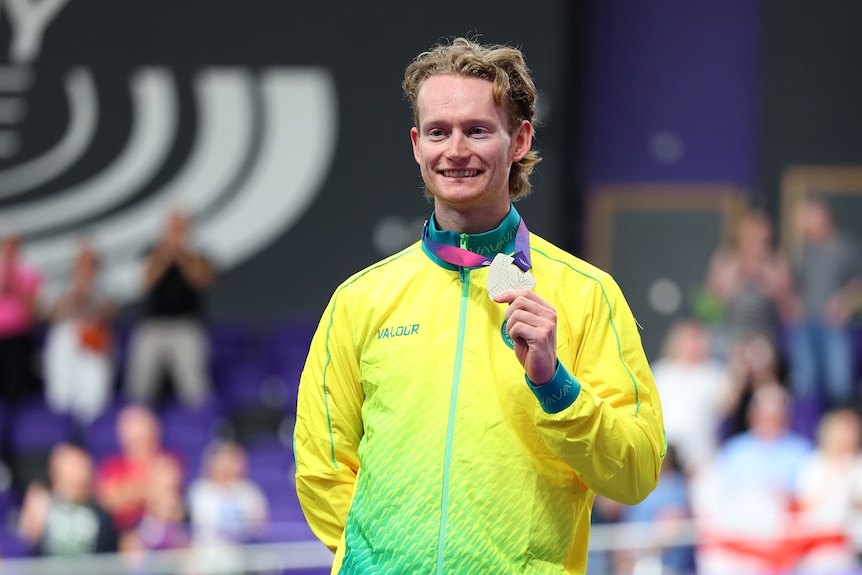 A man smiles while holding his silver medal.