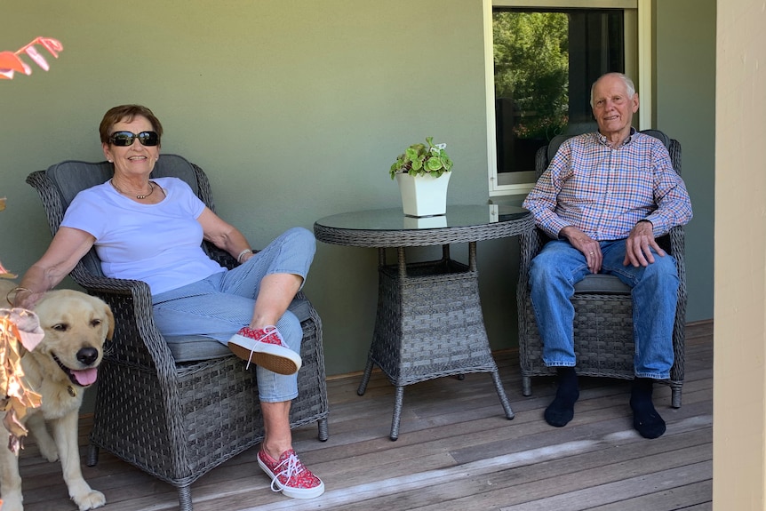 An man and a woman sit on a porch with a dog