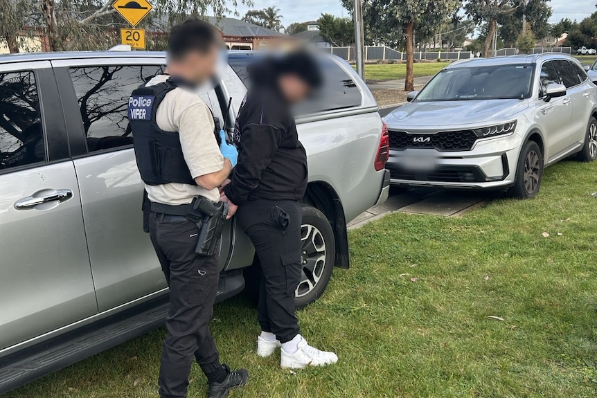 Man under arrest from police officer near cars.