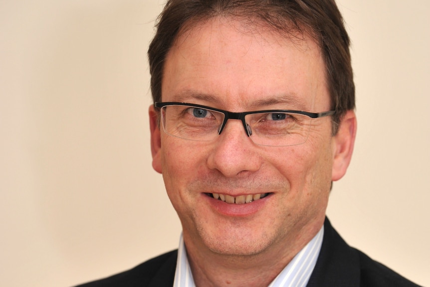 A man with brown hair and glasses smiles.