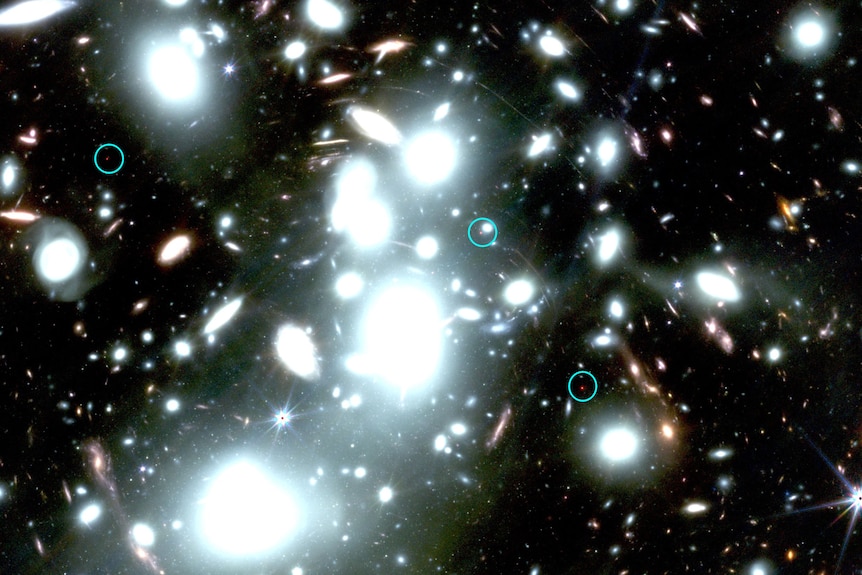 Dark sky with bright white coloured galaxies and blue circles around tiny red dots.
