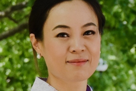 A woman wearing a traditional Korean dress with green leaves in the background.