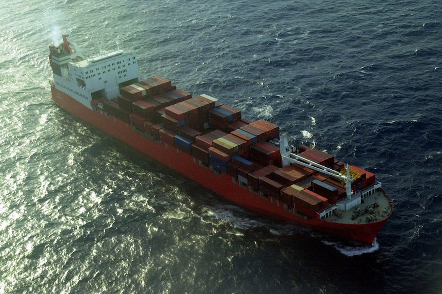 A large red freight ship at sea, with red shipping containers loaded on board.