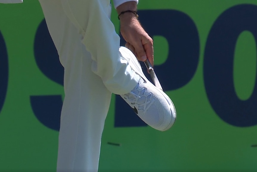 Nathan Lyon clears his cleats with a knife