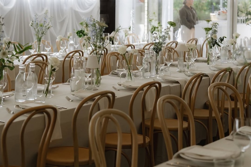 Wedding seating with long white table-clothed tables and floral arrangements under marquee