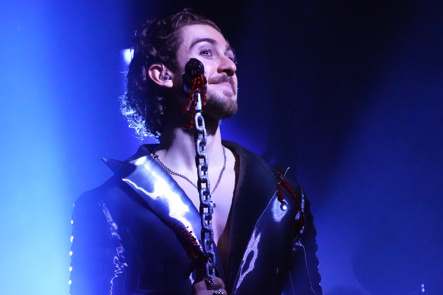 A performing man smiles behind a microphone on stage
