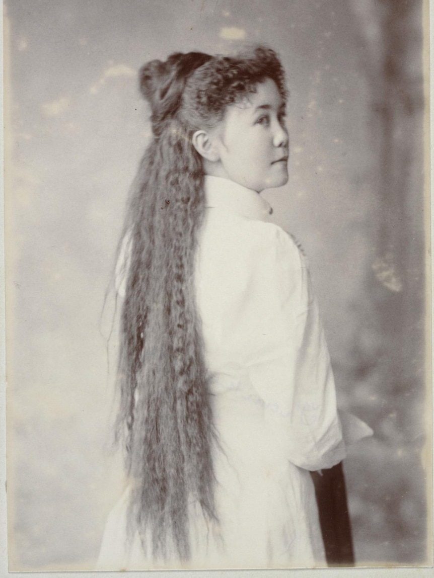 A black and white photo of a woman in the late 1800s, long curly hair down her back.