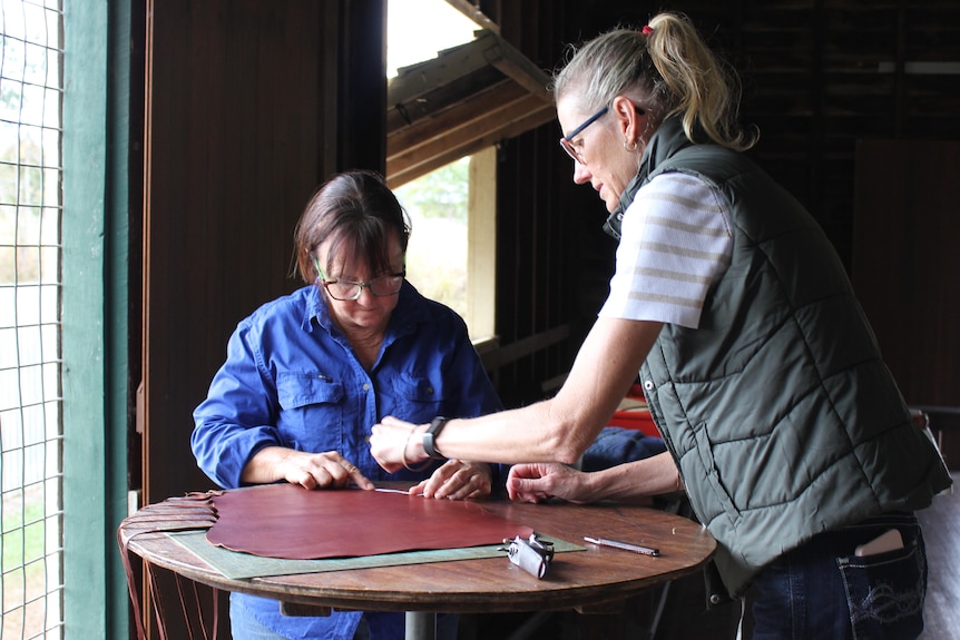 Two women working with pieces of leather at a table