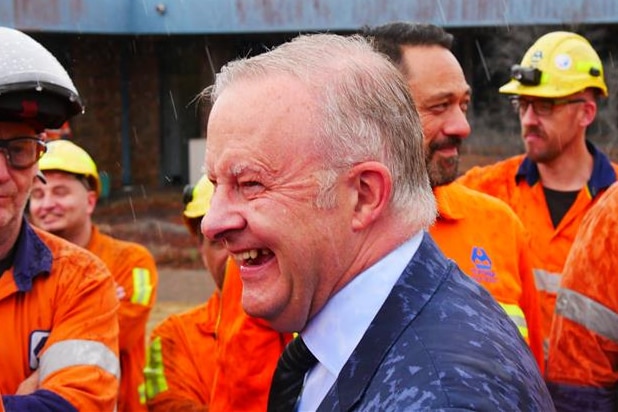 Prime Minister Anthony Albanese laughing in the rain, while talking to Tomago workers dressed in high vis.