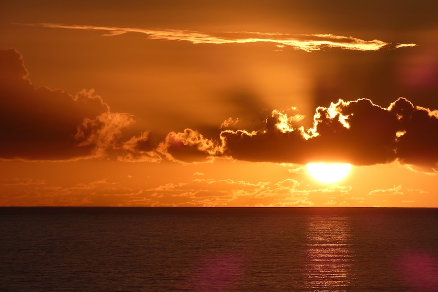 A sunset over the ocean turns the sky orange.