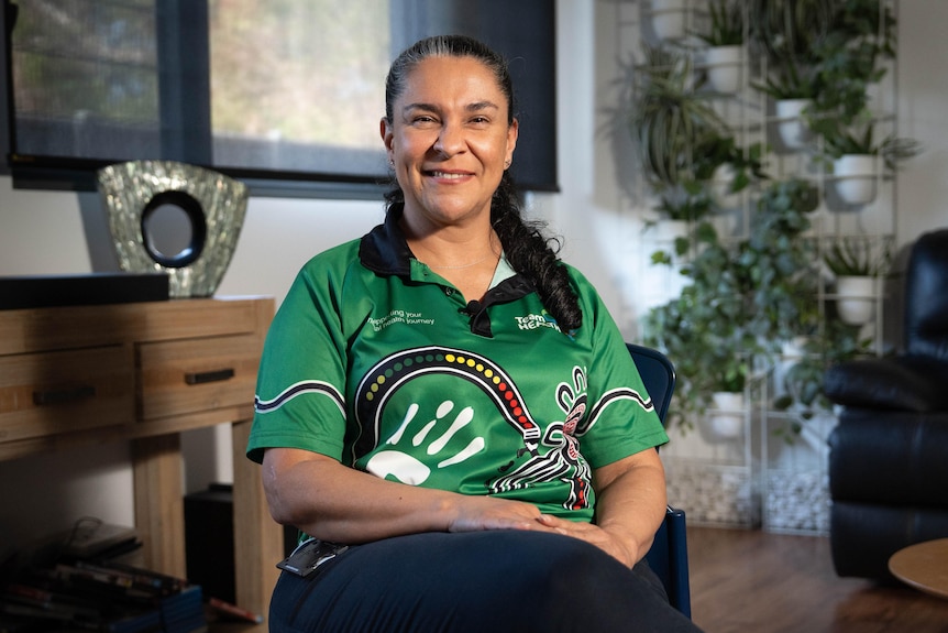Astrid has dark hair is wearing a green TeamHEALTH work shirt, the woman is seated and smiling at the camera.