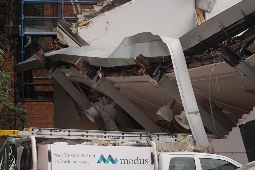 A building partially collapsed on its side onto cars parked in the service station car park.